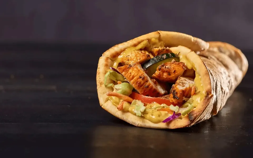 Grilled chicken and fresh vegetables wrapped in a tortilla, drizzled with sauce on a dark background.