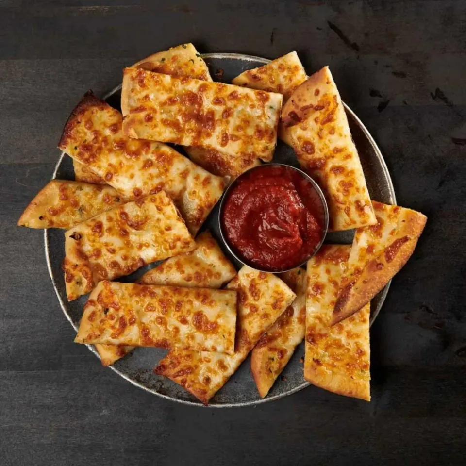 Cheesy breadsticks arranged on a plate with a bowl of marinara sauce in the center.