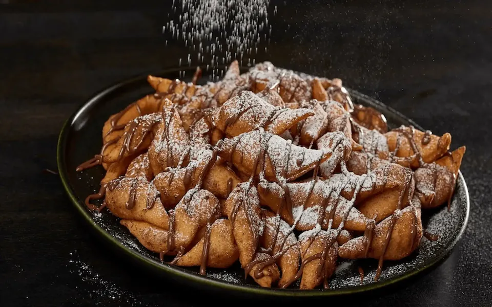 Sugary powder is sprinkled over a plate of chocolate-drizzled pastry twists.