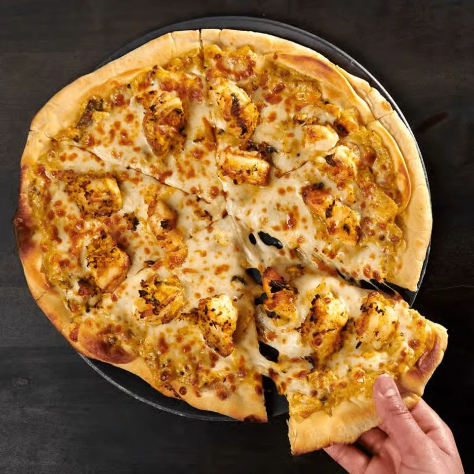 Cheesy pizza with pieces of grilled chicken being pulled from a round platter.