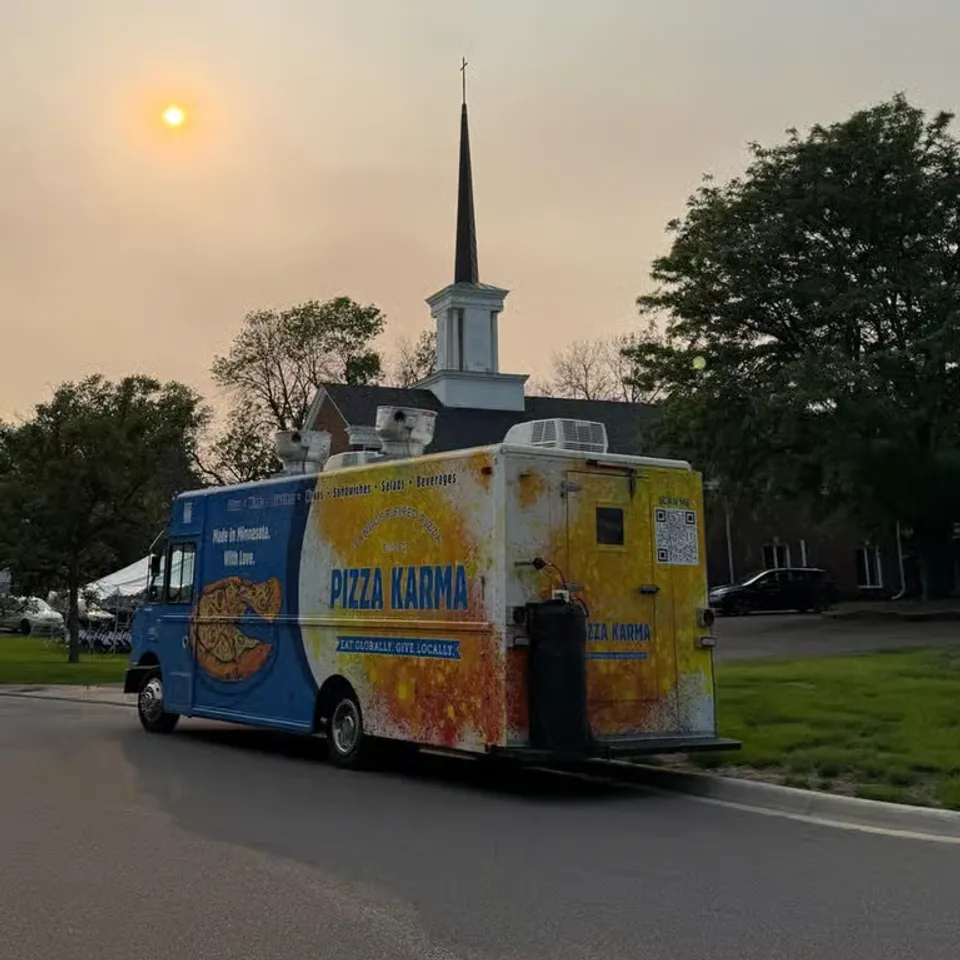 Food truck named "Pizza Karma" parked near a church under a hazy sun.