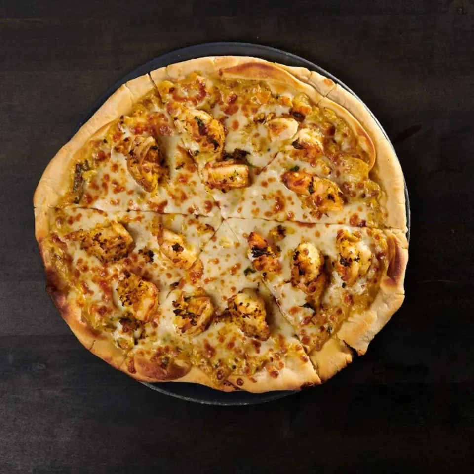 Golden-brown pizza topped with melted cheese and grilled chicken, sliced into eight pieces.