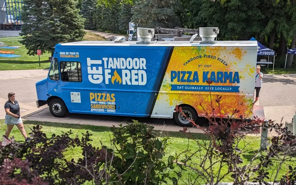 Food truck named "Pizza Karma" parked with a customer walking by in a park setting.