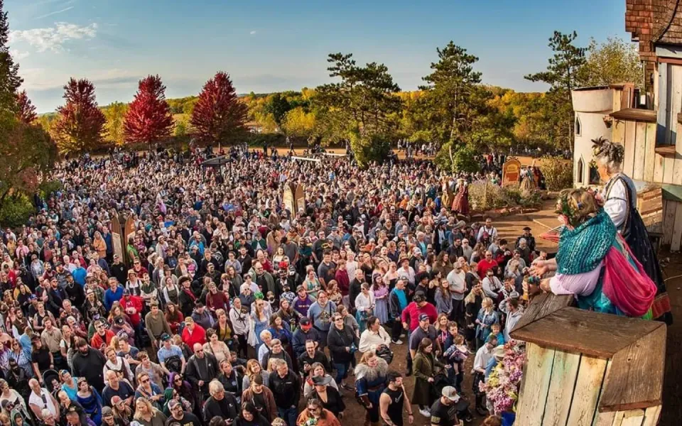 A large crowd gathers outdoors, with costumed performers entertaining from a raised platform.
