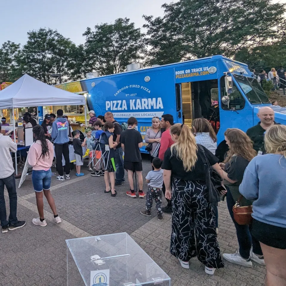 Crowd gathered around a pizza food truck, enjoying the evening atmosphere and waiting in line for food.