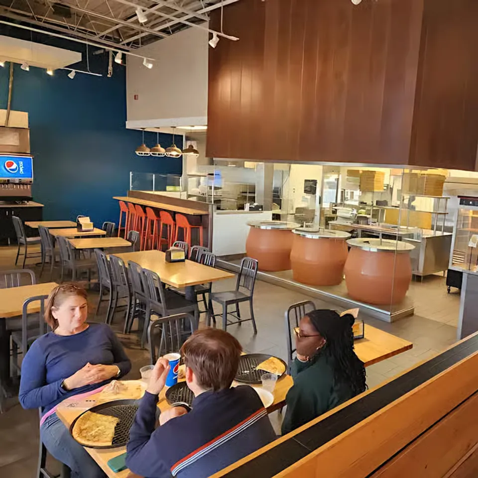 Three patrons seated at a table in a modern restaurant, enjoying food and conversation in a spacious dining area.