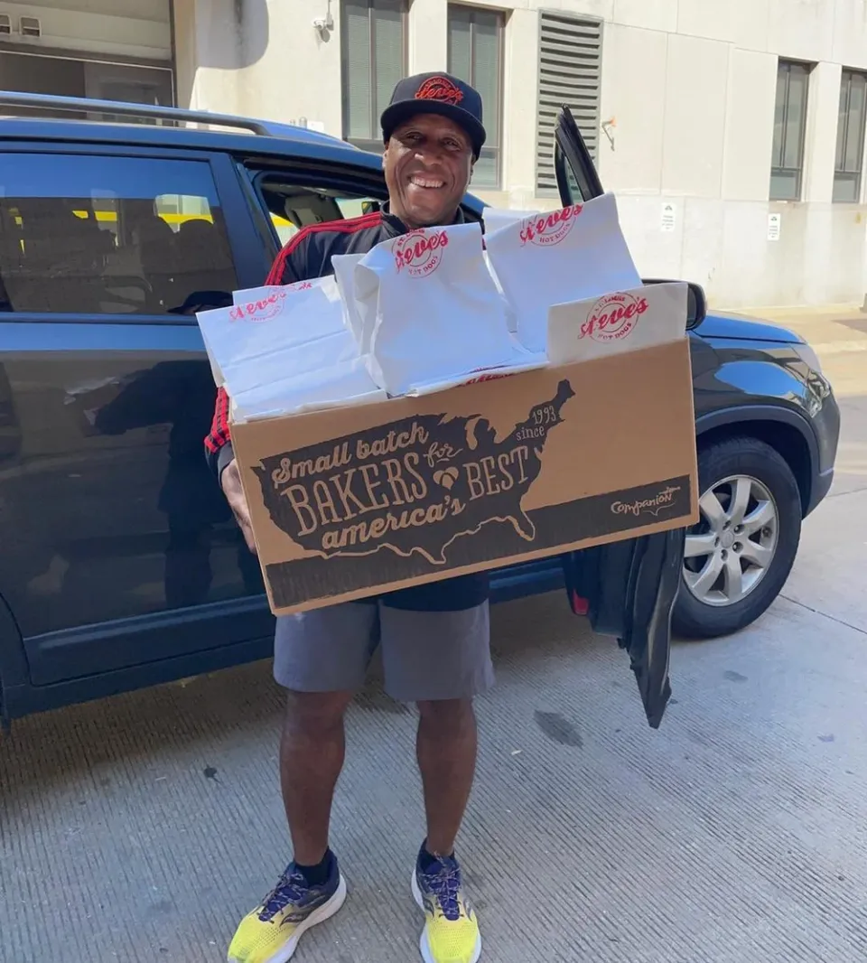 Man smiling while holding a large box and several bags labeled "Steve's," next to a parked car.