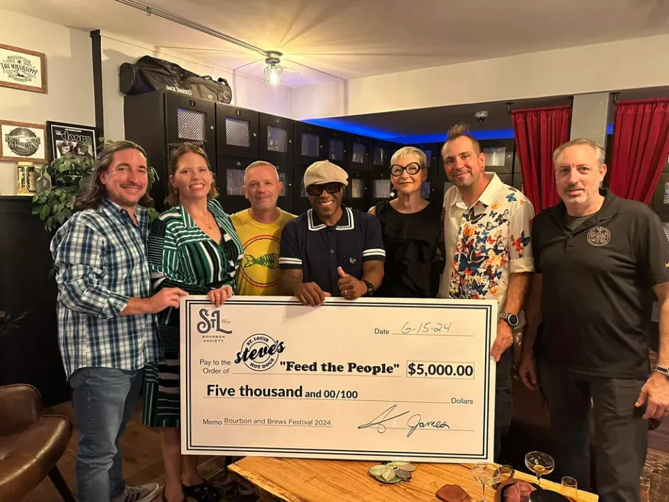 The owners of Steve's Hot Dogs stand with the founders of the St. Louis Bourbon Society with a giant check for a $5,000 donation to the Feed the People Program.