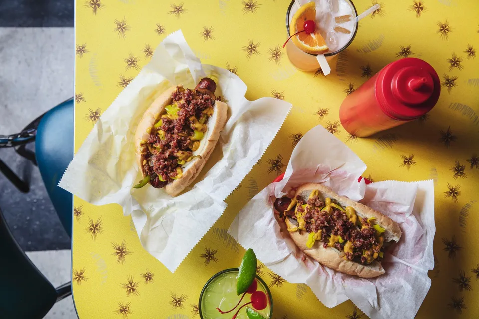 Two St. Louis Style Hot Dogs sit on a yellow table with a ketchup bottle.