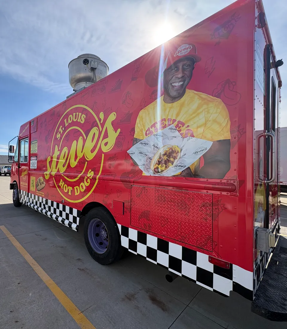 Steve's Hot Dogs food truck is parked. You see a picture of Steve on the food truck holding a hot dog next to a Steve's Hot Dogs logo
